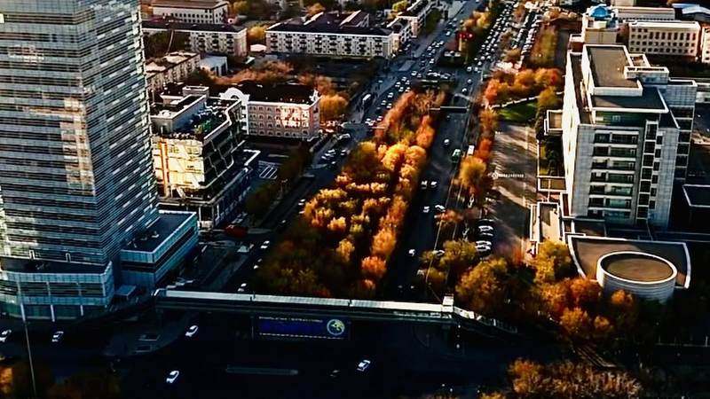 Күздегі Атырау — биік офис ғимараты, сары жапырақты ағаштар және кең көше
